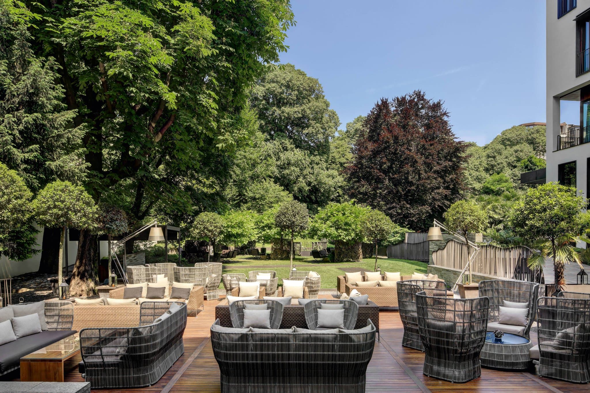 The Bulgari Hotel Milano's private garden at dusk, featuring the black resin oval bar and guests enjoying aperitivo under white umbrellas.