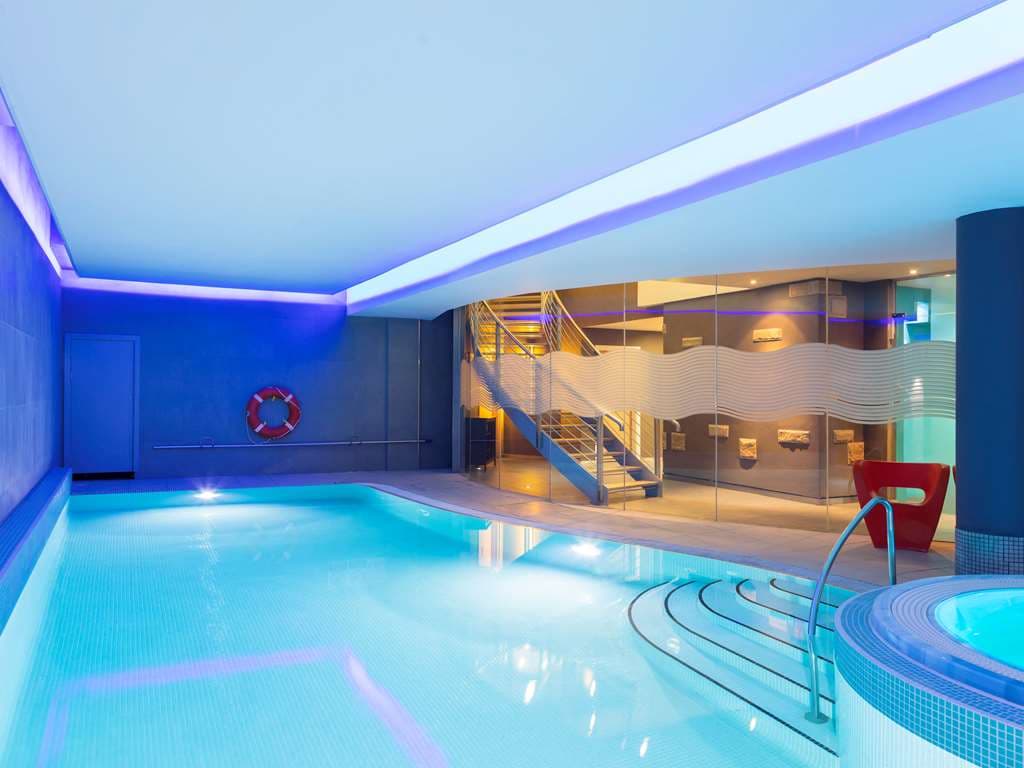 Indoor swimming pool at Novotel Edinburgh Centre illuminated by blue mood lighting, with lounge chairs in the background.