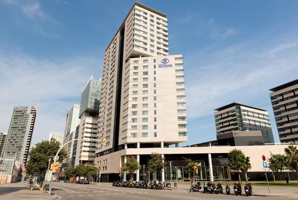 White sunbeds and blue pool water at Purobeach Barcelona club at Hilton Diagonal Mar under a clear sky.