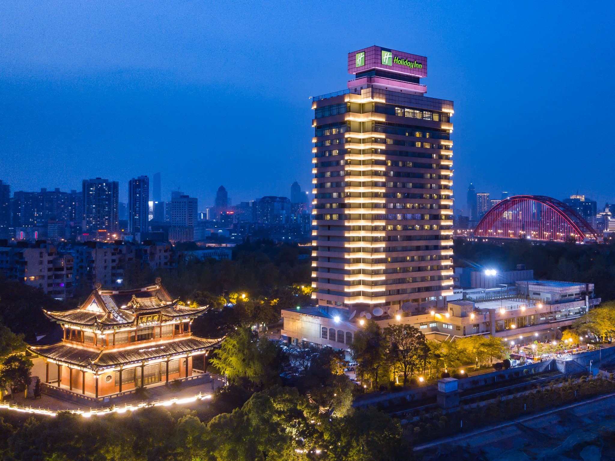 A guest sitting on a window ledge in the Holiday Inn Wuhan Riverside, looking out at the illuminated Yangtze River Bridge and Yellow Crane Tower in the distance.