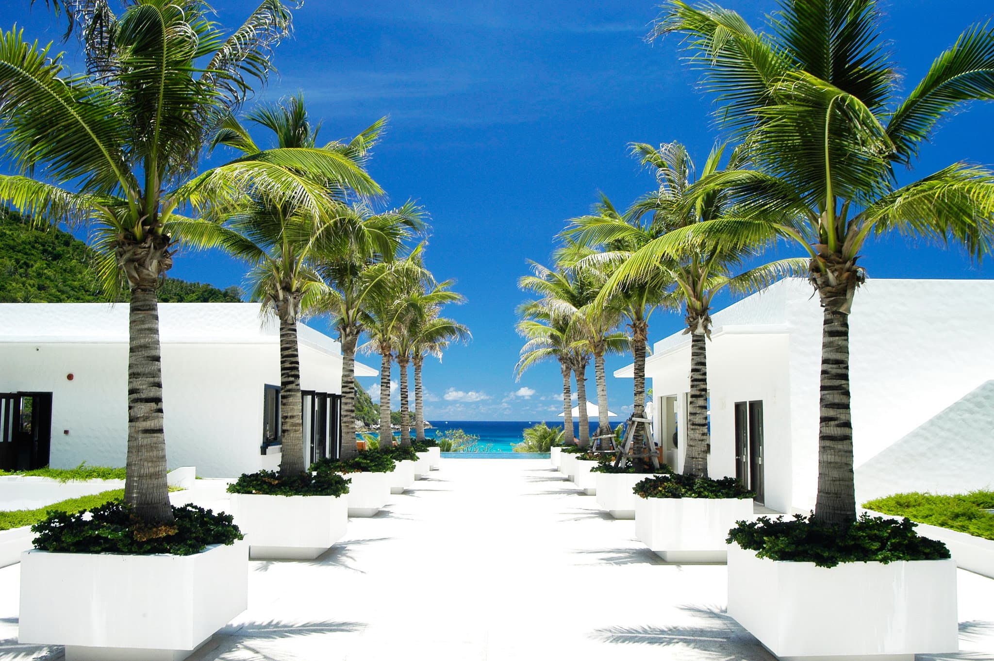 Aerial view of The Racha's white minimalist villas contrasting with the turquoise Andaman Sea and Batok Bay.