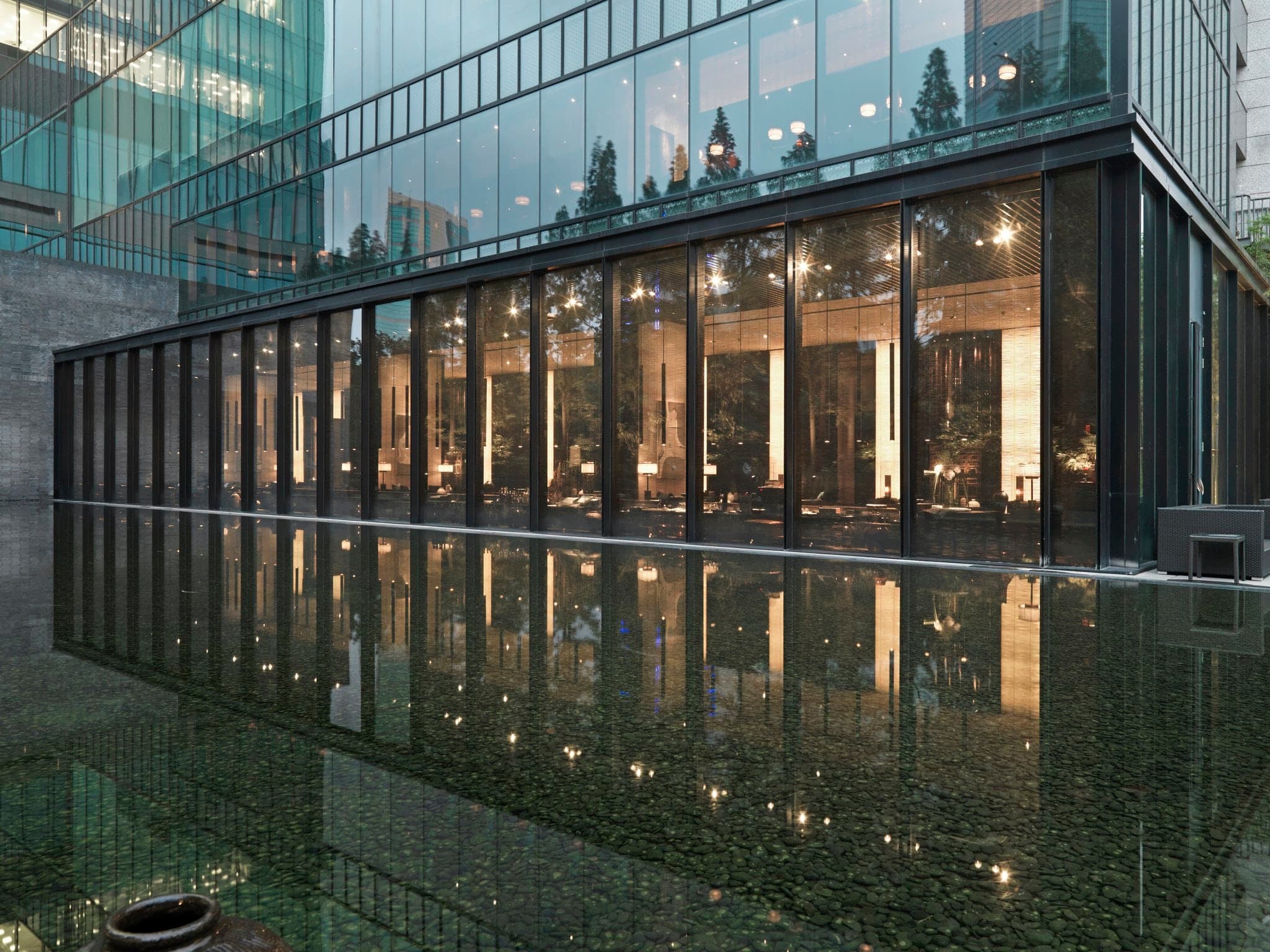 The PuLi Hotel's 32-meter solid teak Long Bar illuminated by low-hanging lanterns in a dimly lit, minimalist lobby.