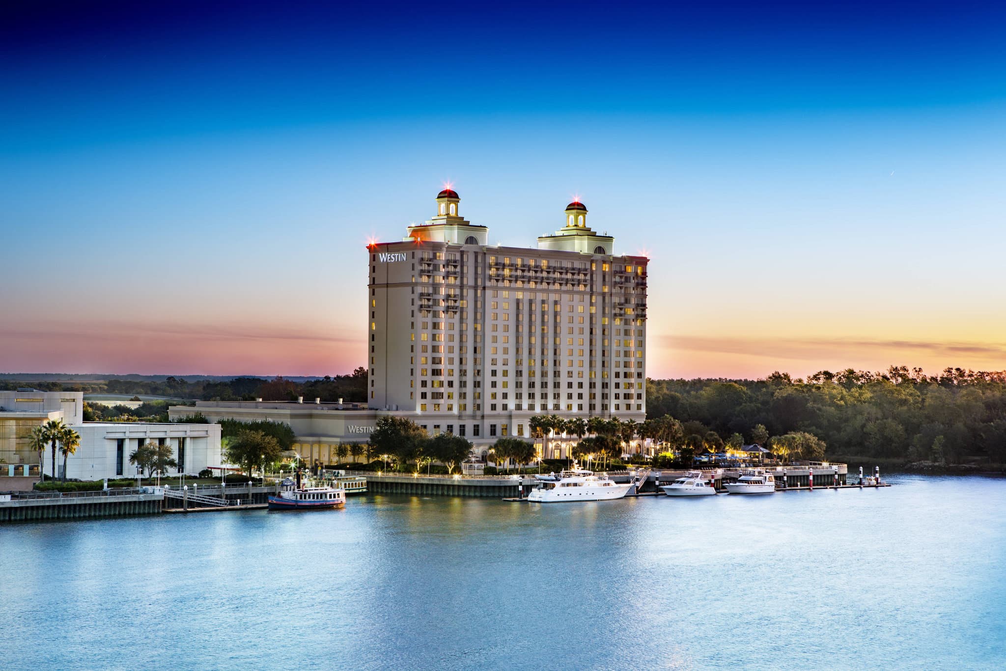The Westin Savannah Harbor exterior at dusk featuring the large riverfront pool and the Savannah skyline in the background.