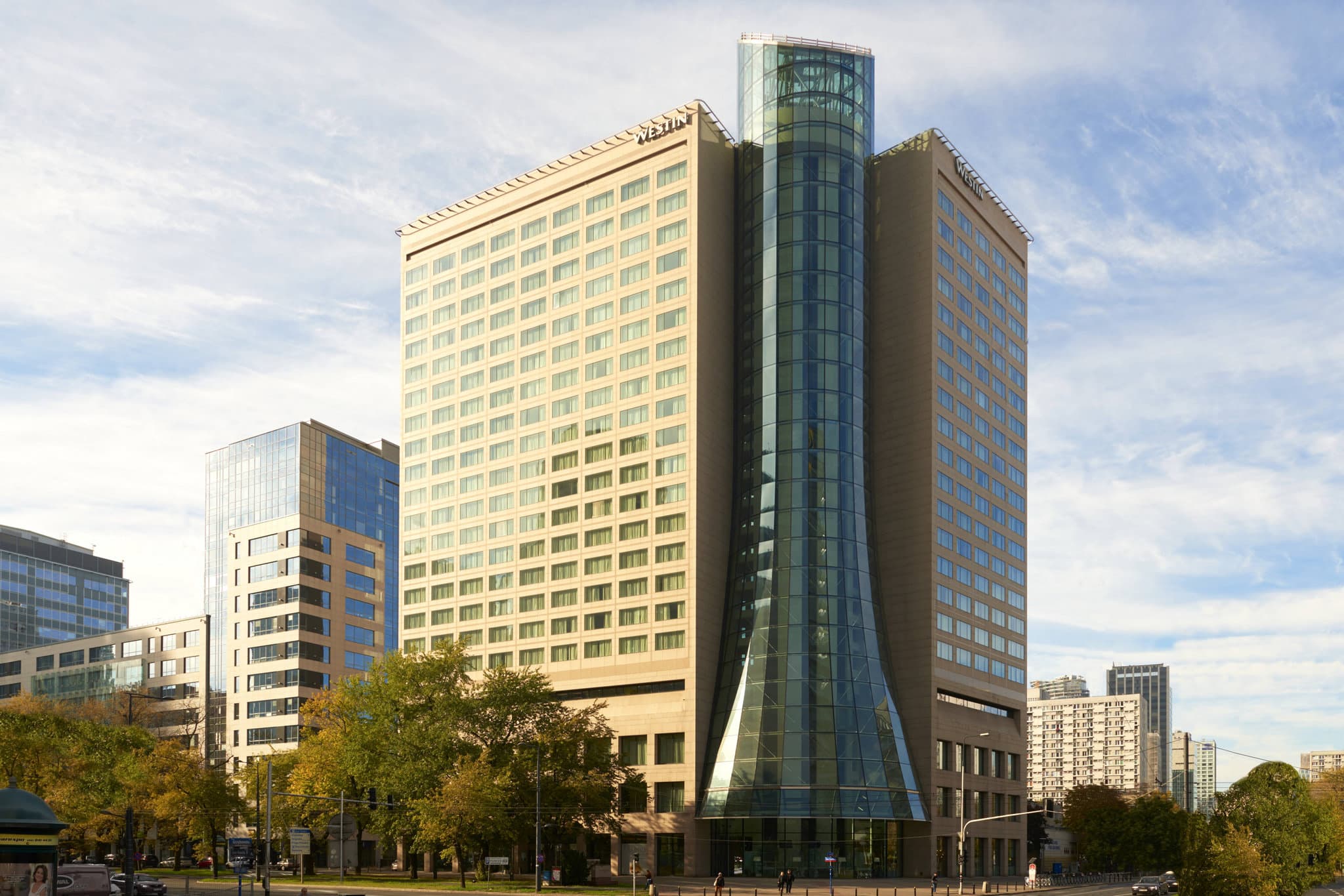 Night view of The Westin Warsaw featuring the illuminated panoramic glass elevator shaft glowing against the dark city skyline.