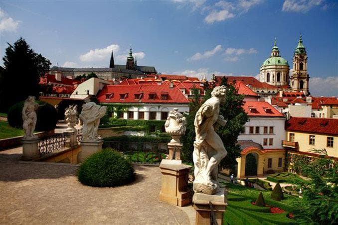 View from Aria Hotel rooftop terrace featuring the massive green dome of St. Nicholas Church and Prague Castle spires at sunset.