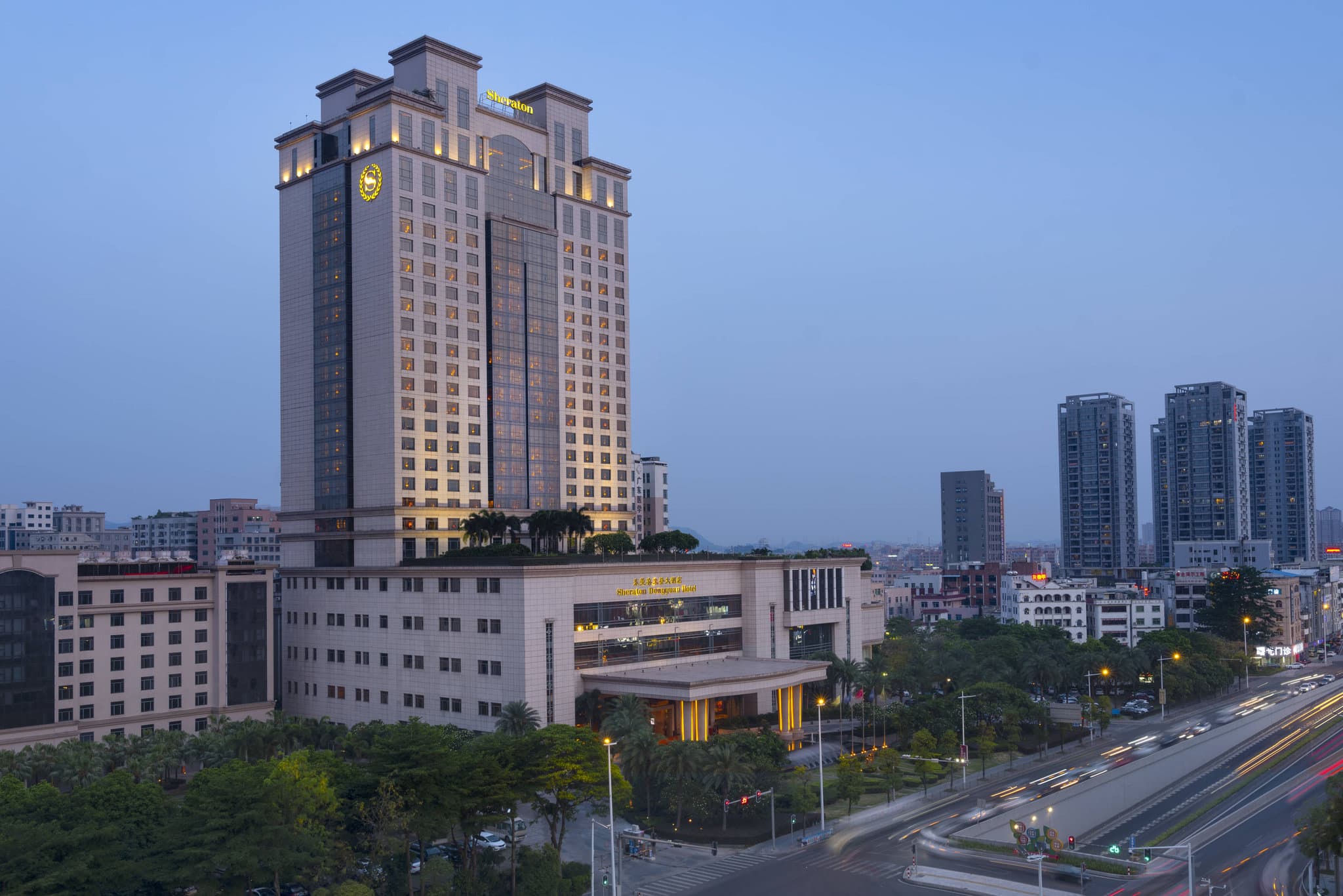 A high-angle view of the Sheraton Dongguan's sprawling outdoor pool complex surrounded by lush palm trees and the Belt Collins landscaped gardens.