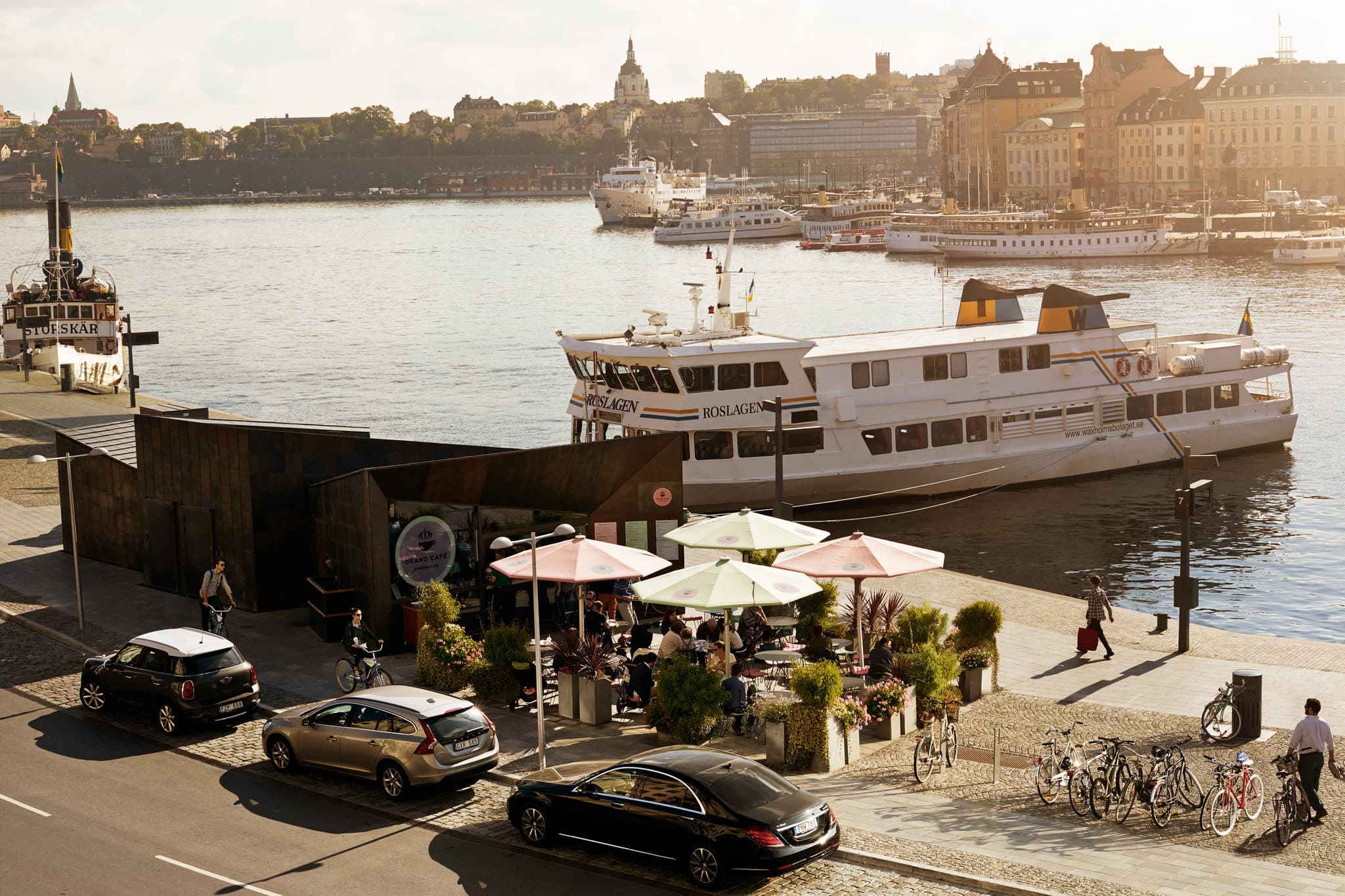 The iconic yellow facade of Grand Hôtel Stockholm reflecting in the harbor at sunset, with boats docked in the foreground.