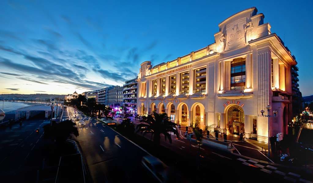 The imposing 1929 Art Deco façade of Hyatt Regency Nice Palais de la Méditerranée illuminated at dusk, framing the third-floor terrace and pool.