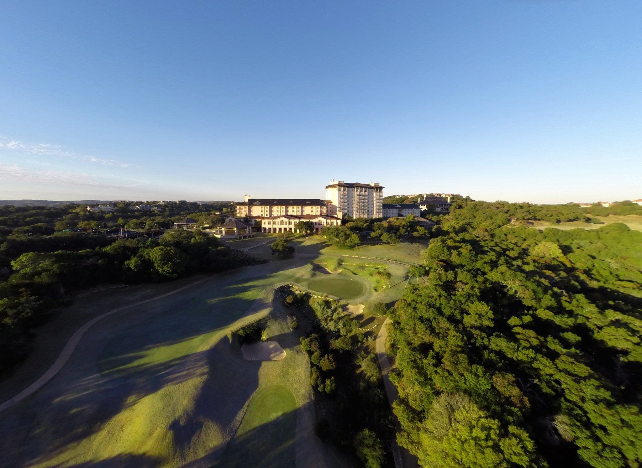 A sweeping view of the Omni Barton Creek infinity pool overlooking the lush green Fazio Foothills golf course at sunset.