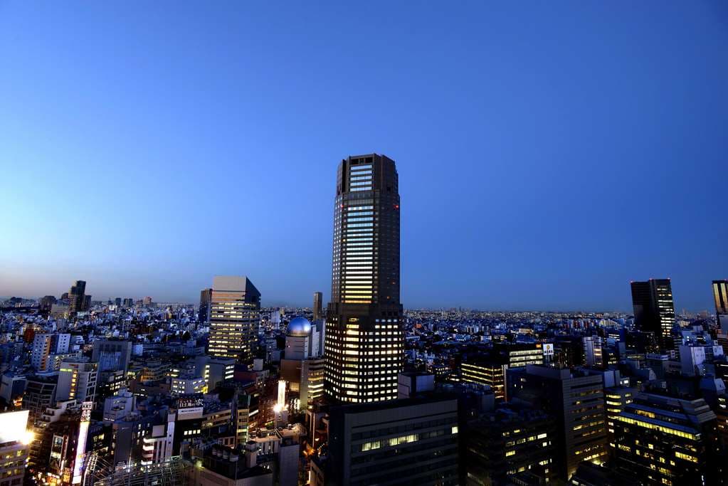 Silhouette of a martini glass at Tower's Bar Bellovisto against a backdrop of Tokyo night lights and Shibuya Scramble.