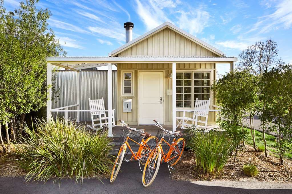 A standalone white cottage with a corrugated metal roof and a private front porch with rocking chairs at Carneros Resort.