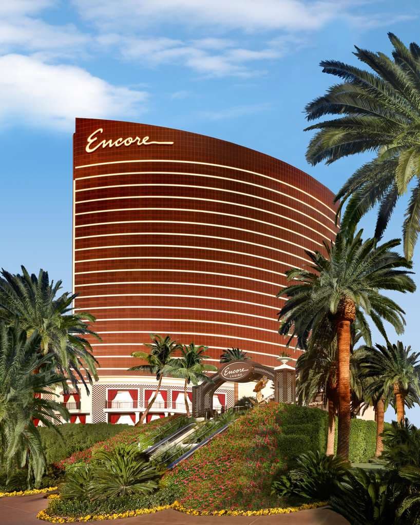 A view from a Wynn Fairway Villa balcony overlooking the lush golf course and the curved bronze hotel tower under a blue sky.