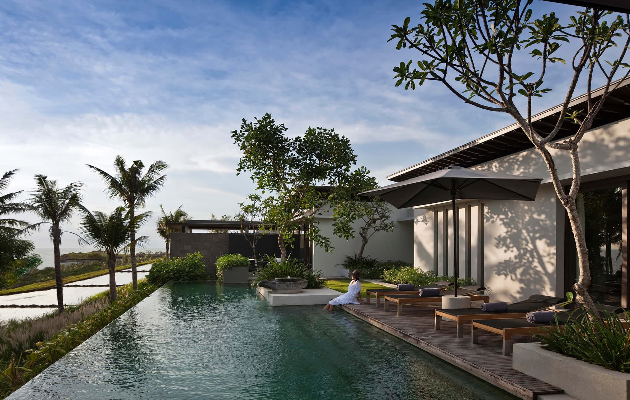 A dramatic infinity pool edge leading to a vast black sand beach with violent ocean waves and a moody grey sky at Soori Bali.