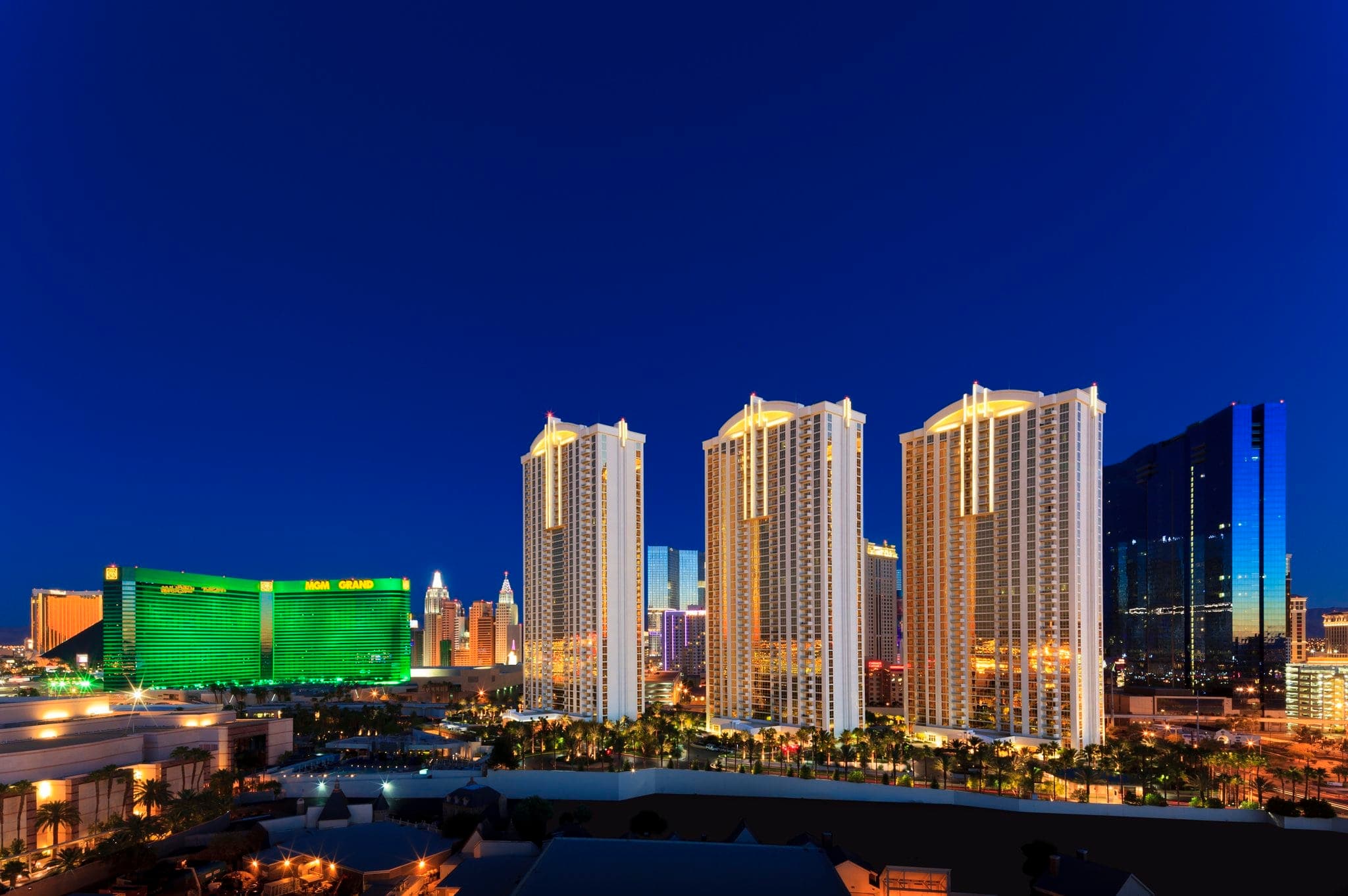 A guest standing on a private balcony at The Signature Las Vegas at twilight, looking out over the glowing green MGM Grand and the Las Vegas Strip skyline.