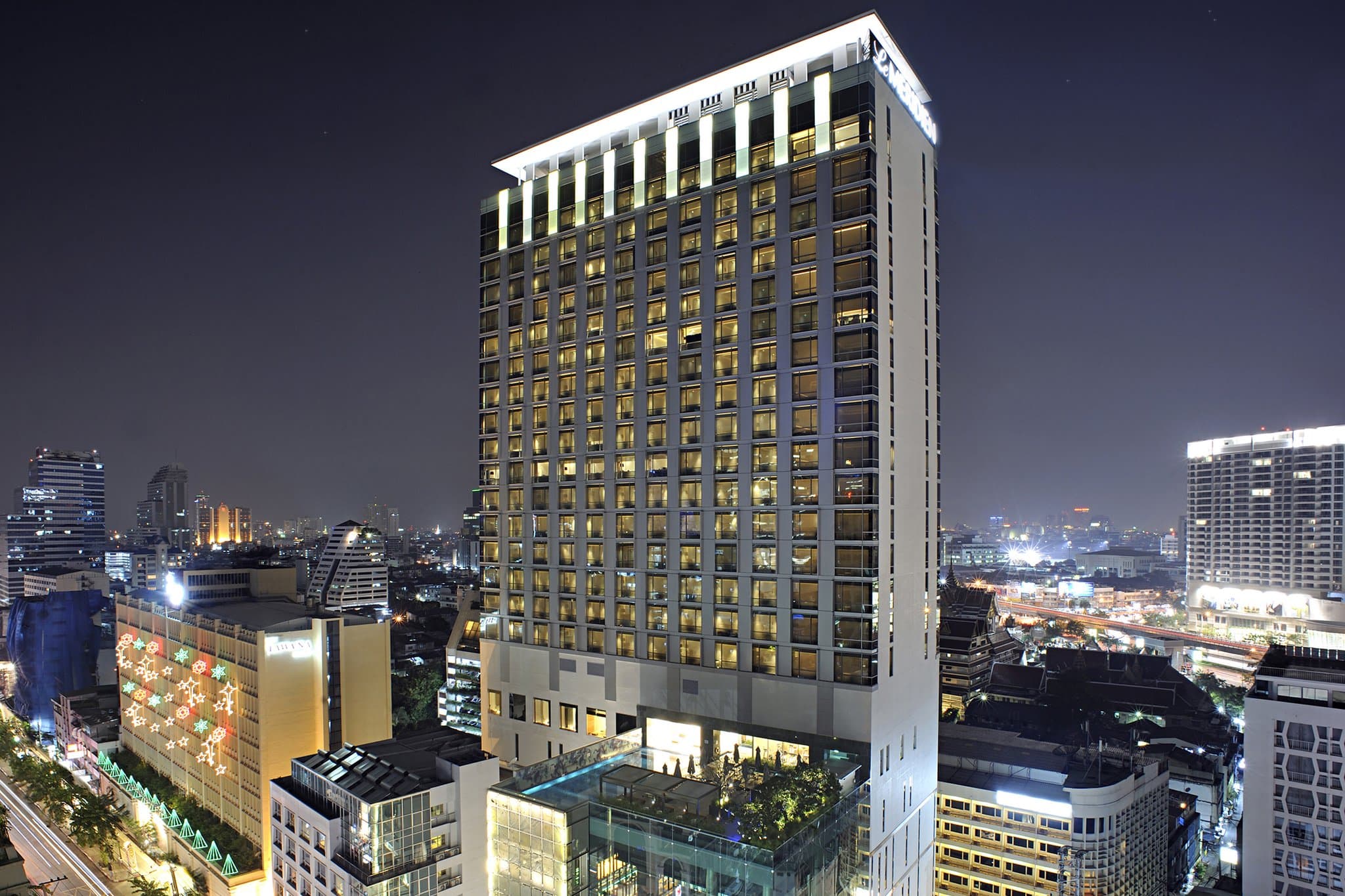 A giant white 'I-Jud' dog sculpture standing at the entrance of Le Méridien Bangkok, with a modern glass facade in the background.