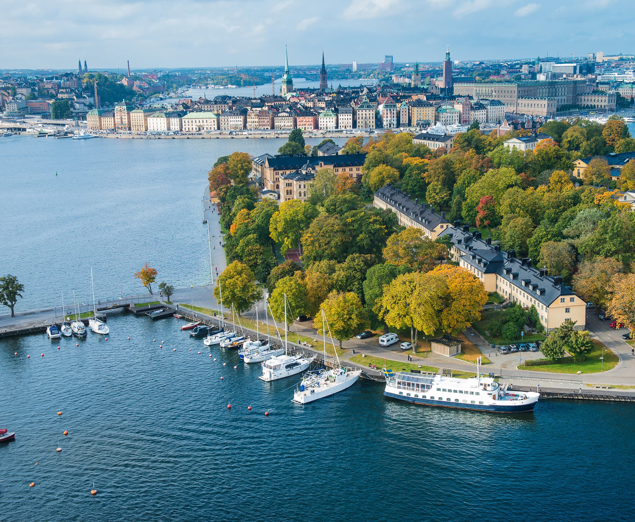 Hotel Skeppsholmen's yellow 1699 facade seen from the park with the gilded crown of Skeppsholmsbron bridge in the background.
