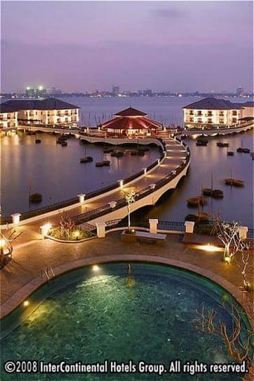 White overwater pavilions of InterContinental Hanoi Westlake glowing at twilight, connected by wooden boardwalks over the lake.