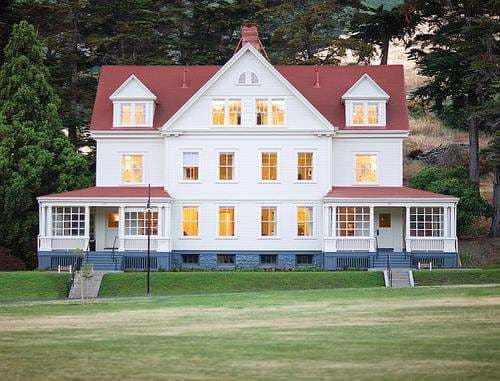 A wide shot of Cavallo Point's white colonial officers' quarters with green roofs, with the Golden Gate Bridge looming in the foggy background.
