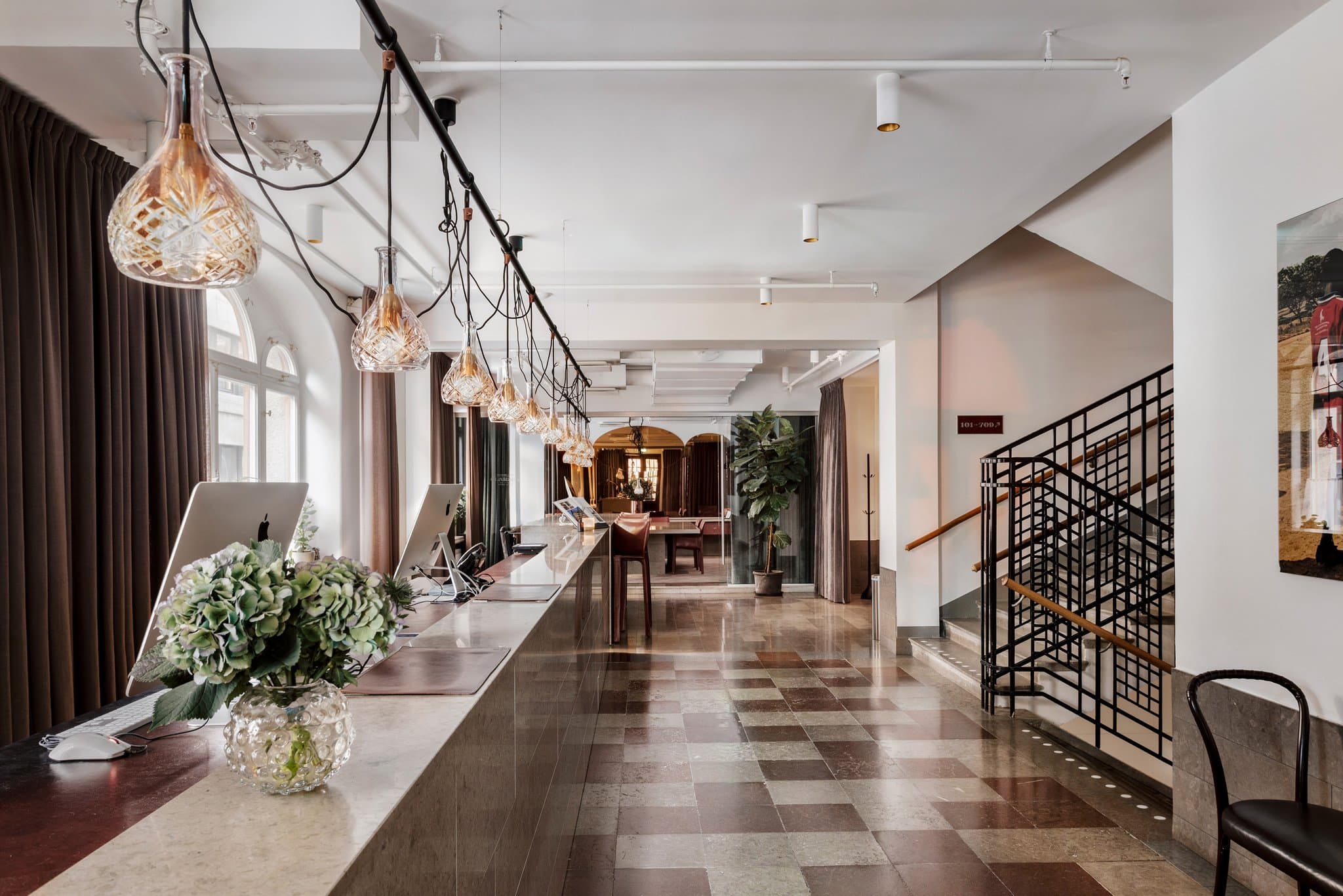 A moody, minimalist hotel room at Miss Clara featuring dark herringbone floors, bentwood chairs, and a large arched window with a deep limestone sill.