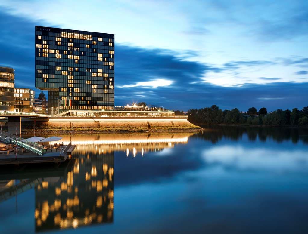 View of the Hyatt Regency Dusseldorf glass facade at twilight, reflecting the lights of the MedienHafen and the Rhine Tower.