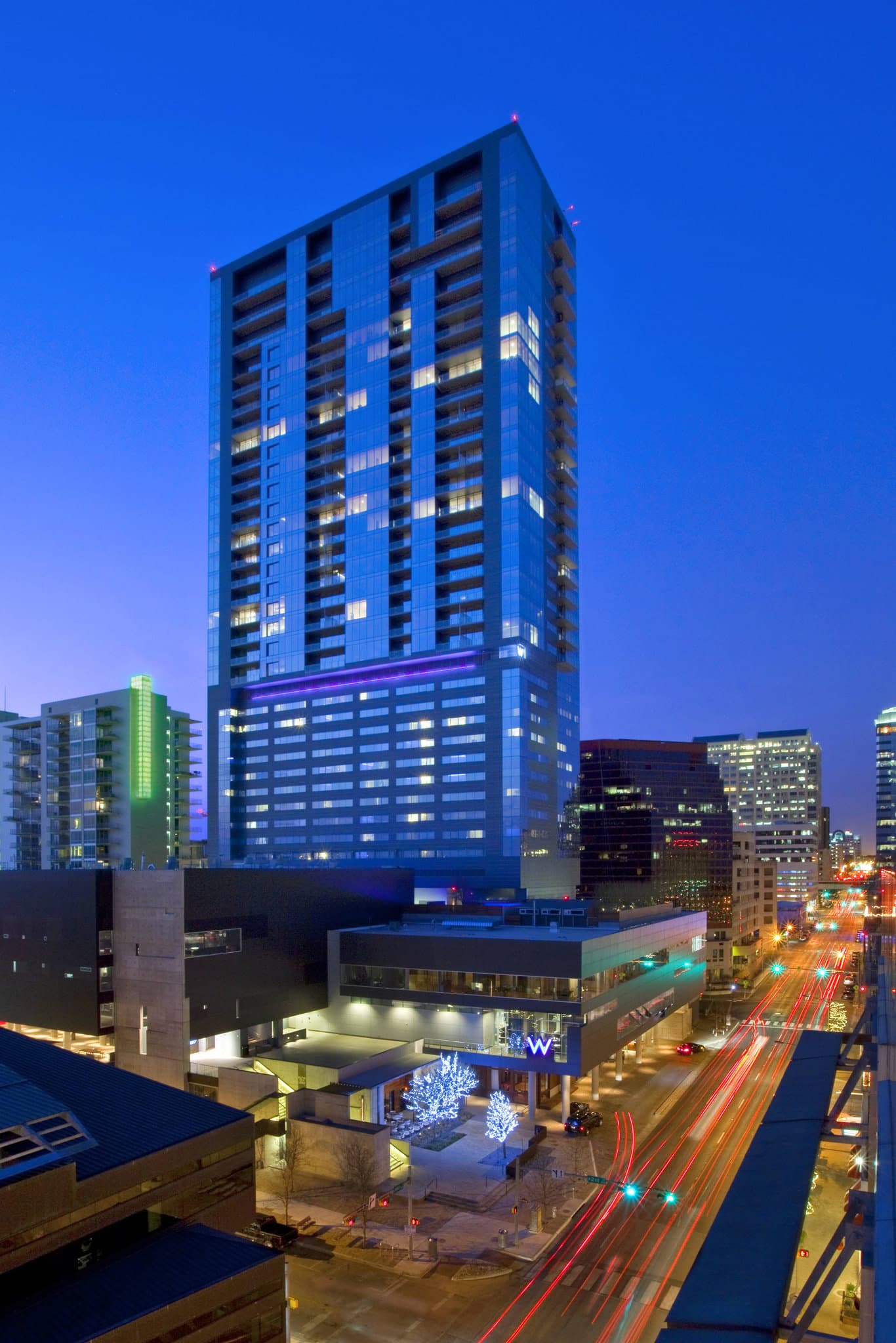 The W Austin WET Deck pool at twilight with guests mingling in cabanas against the downtown Austin skyline.