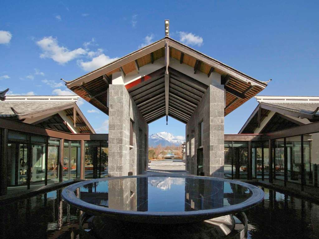 A serene reflection pool at Pullman Lijiang framing the snow-capped Jade Dragon Snow Mountain under a blue sky.