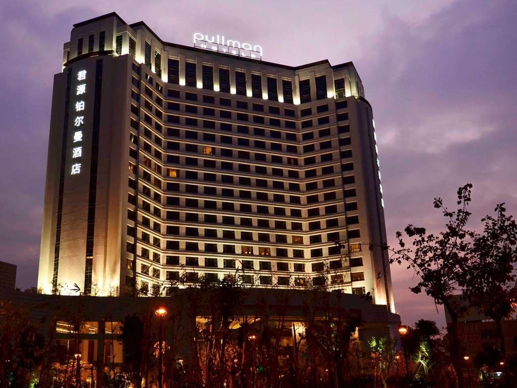Lobby of Pullman Dongguan Changan featuring towering geometric wooden lattice screens and warm mood lighting.