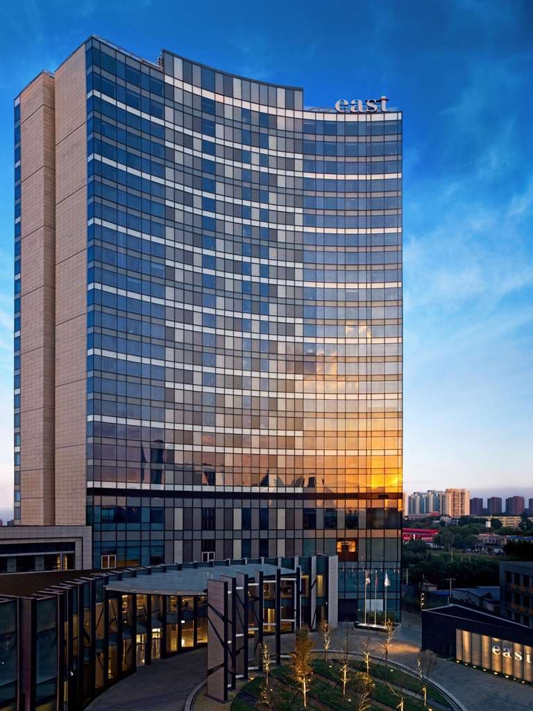 大きな窓から街の景色を望む、EAST Beijingの洗練されたモダンな客室。ミニマルな木製家具と柔らかな間接照明が特徴。