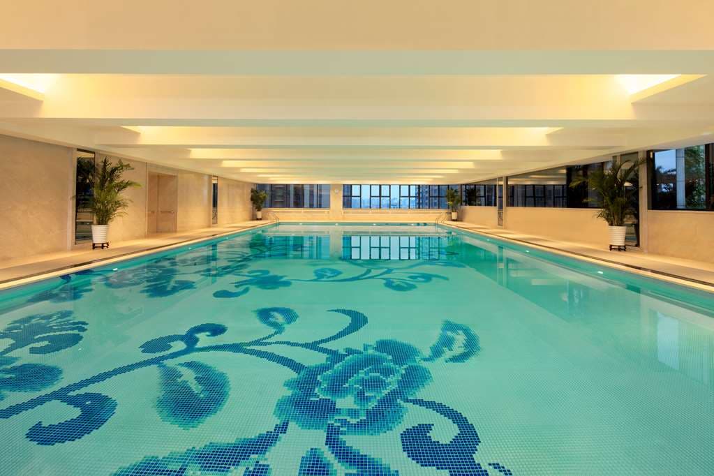Silhouette of a guest standing before the Hilton Foshan's massive, glowing lobby aquarium.