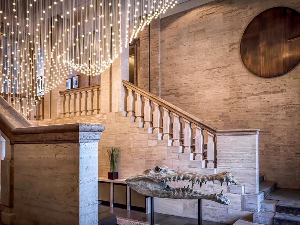 A chic hotel bar lounge featuring yellow sofas and large panoramic windows looking directly into a green ostrich enclosure at the Berlin Zoo.