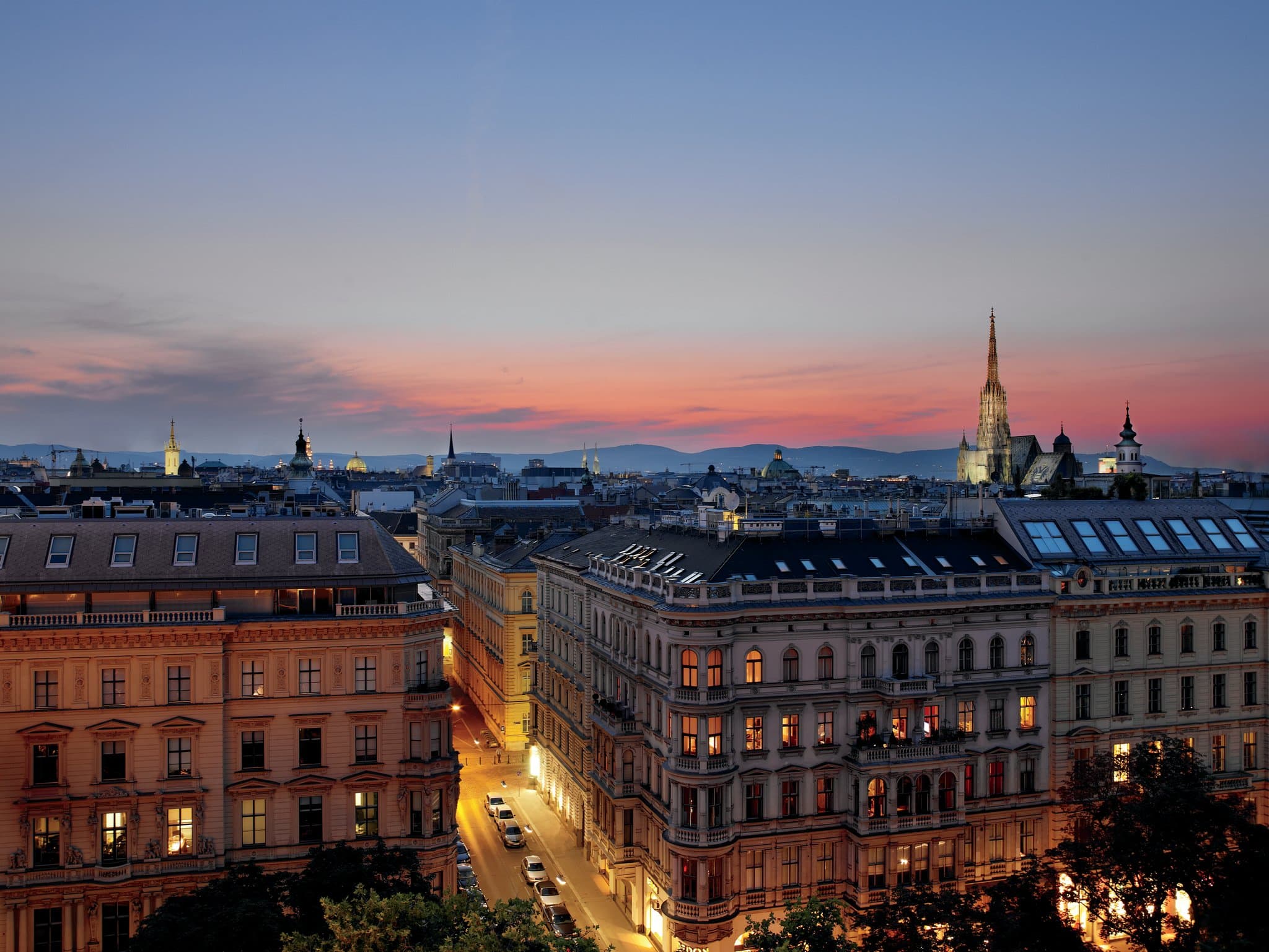 The Ritz-Carlton Vienna Atmosphere Rooftop Bar at sunset with St. Stephen's Cathedral spire in the background.