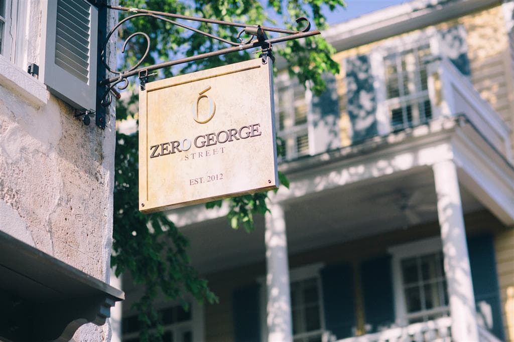 The oyster-shell paved courtyard of Zero George Street at dusk, illuminated by gas lanterns with white piazzas in the background.