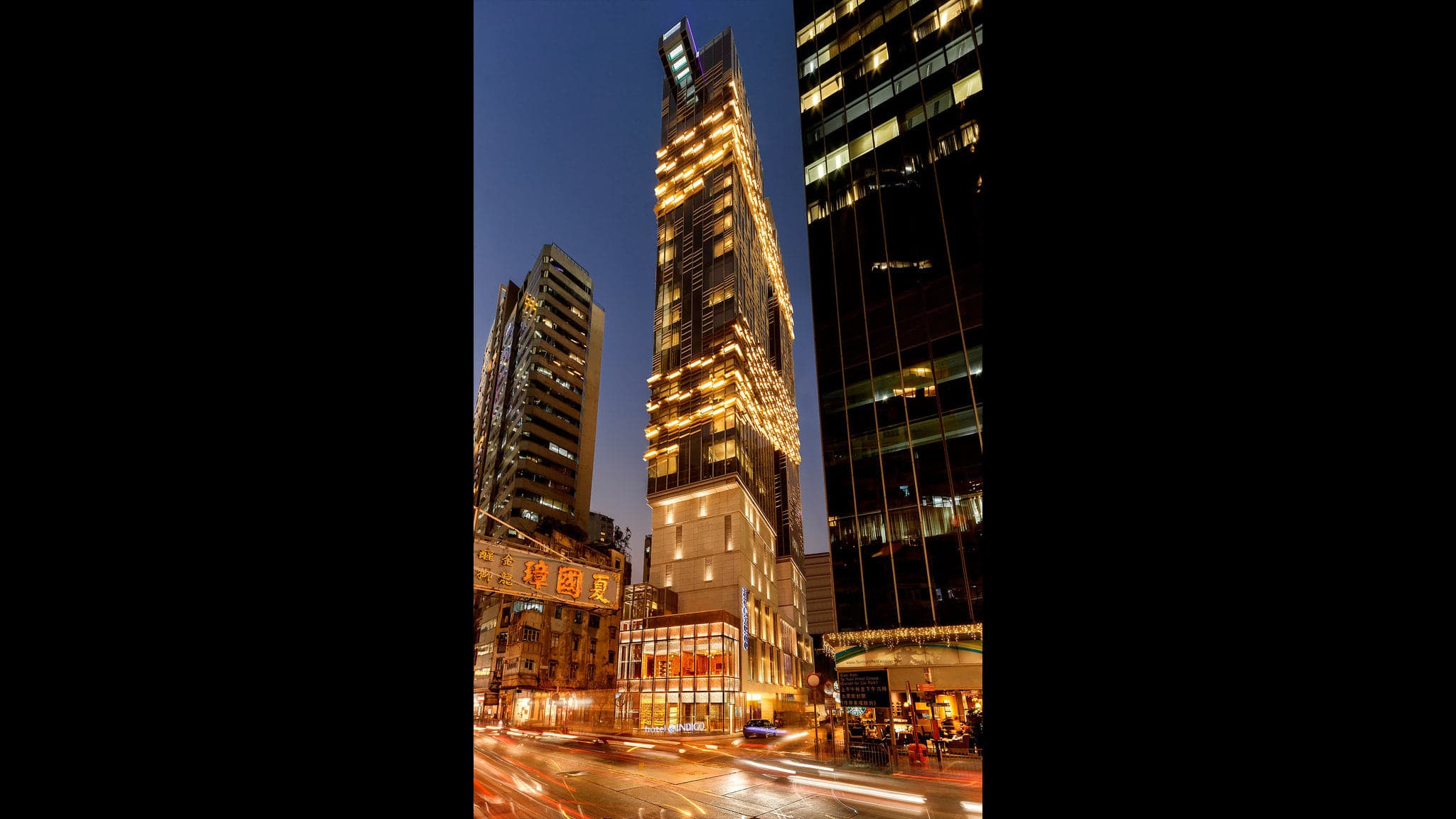 The bronze dragon-scale facade of Hotel Indigo Hong Kong Island glowing at twilight.