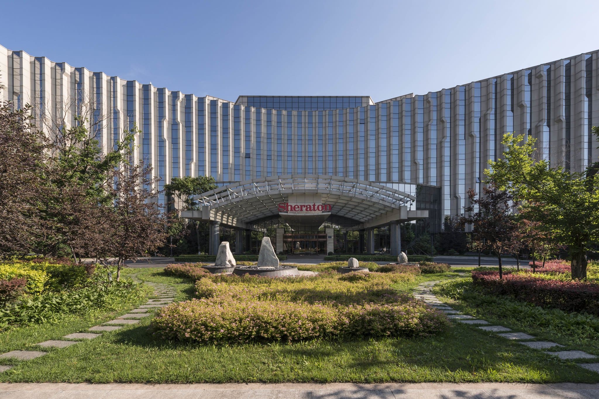 Sheraton Changchun Jingyuetan Hotel exterior surrounded by dense forest and snow, featuring modern architecture against a natural landscape.
