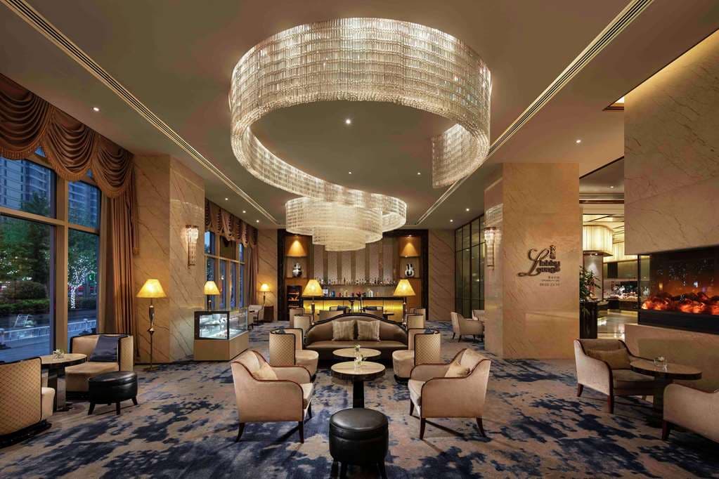 High-ceilinged lobby lounge of Hilton Zhengzhou featuring crystal chandeliers and a grand staircase.