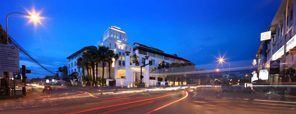 The central courtyard of Park Hyatt Siem Reap featuring a large ancient Banyan tree, illuminated at twilight with Art Deco architectural details.