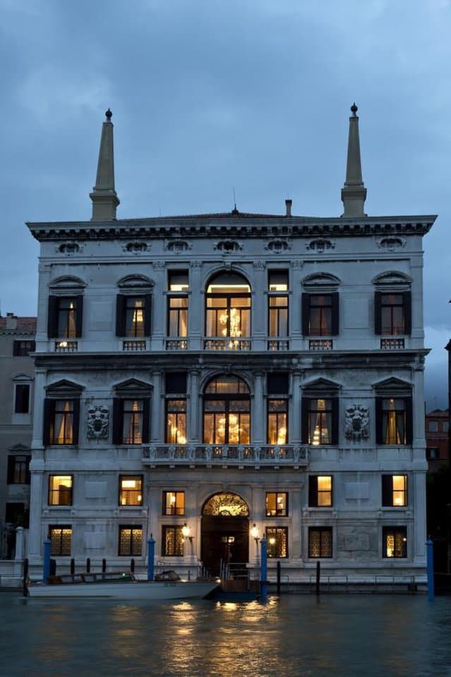 The opulent Piano Nobile ballroom at Aman Venice featuring original Tiepolo frescoes, gilded Rococo moldings, and tall windows overlooking the Grand Canal.
