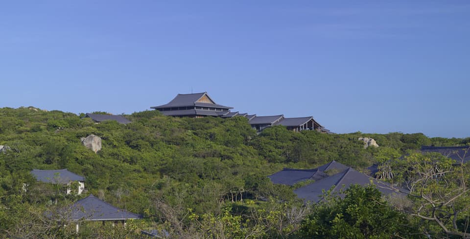 Amanoi's infinity Cliff Pool overlooking the dramatic coastline of Vinh Hy Bay at sunrise, framed by lush jungle and grey granite boulders.