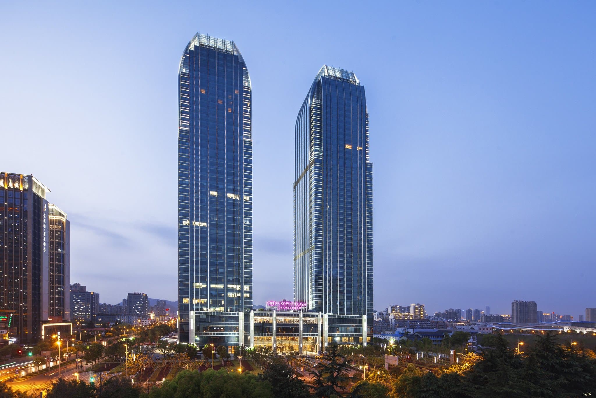 A dramatic silhouette of the Crowne Plaza Wuxi Taihu twin towers reflecting in the Lihu Lake at twilight.