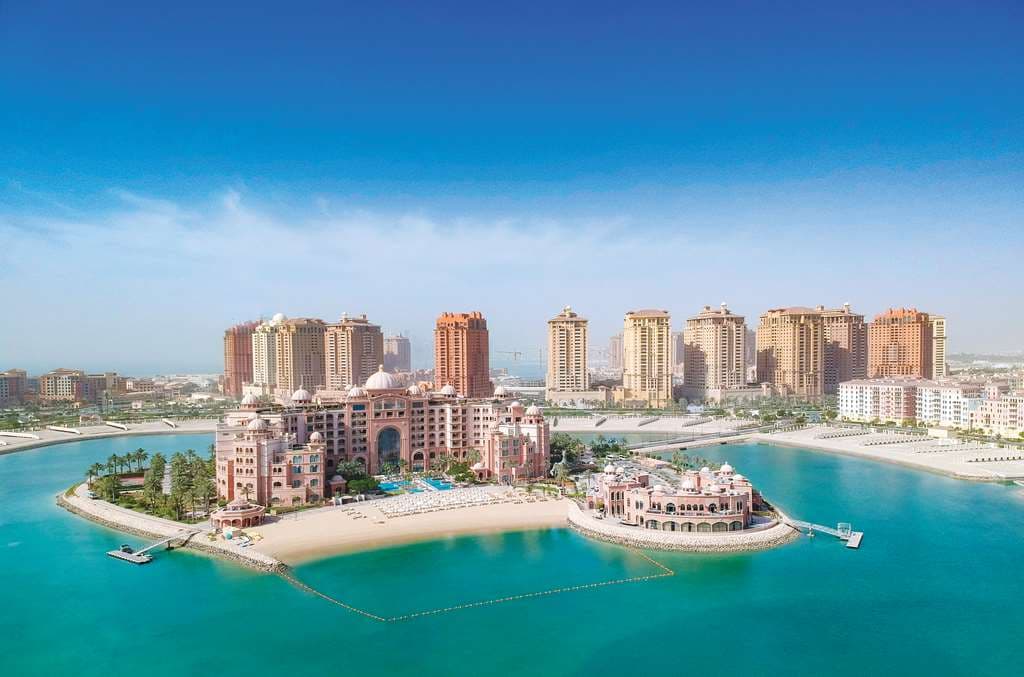 The palatial exterior of Marsa Malaz Kempinski at night, illuminated against the dark water of The Pearl-Doha, featuring grand domes and arched windows.