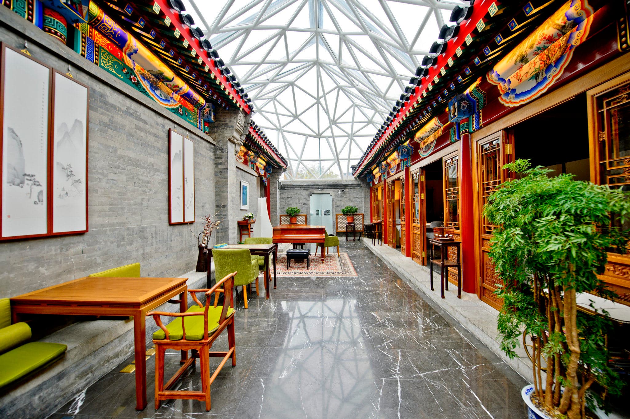 A dramatic glass-roofed atrium at Cours Et Pavillons casting shadows on traditional grey stone floors and carved wooden pillars.