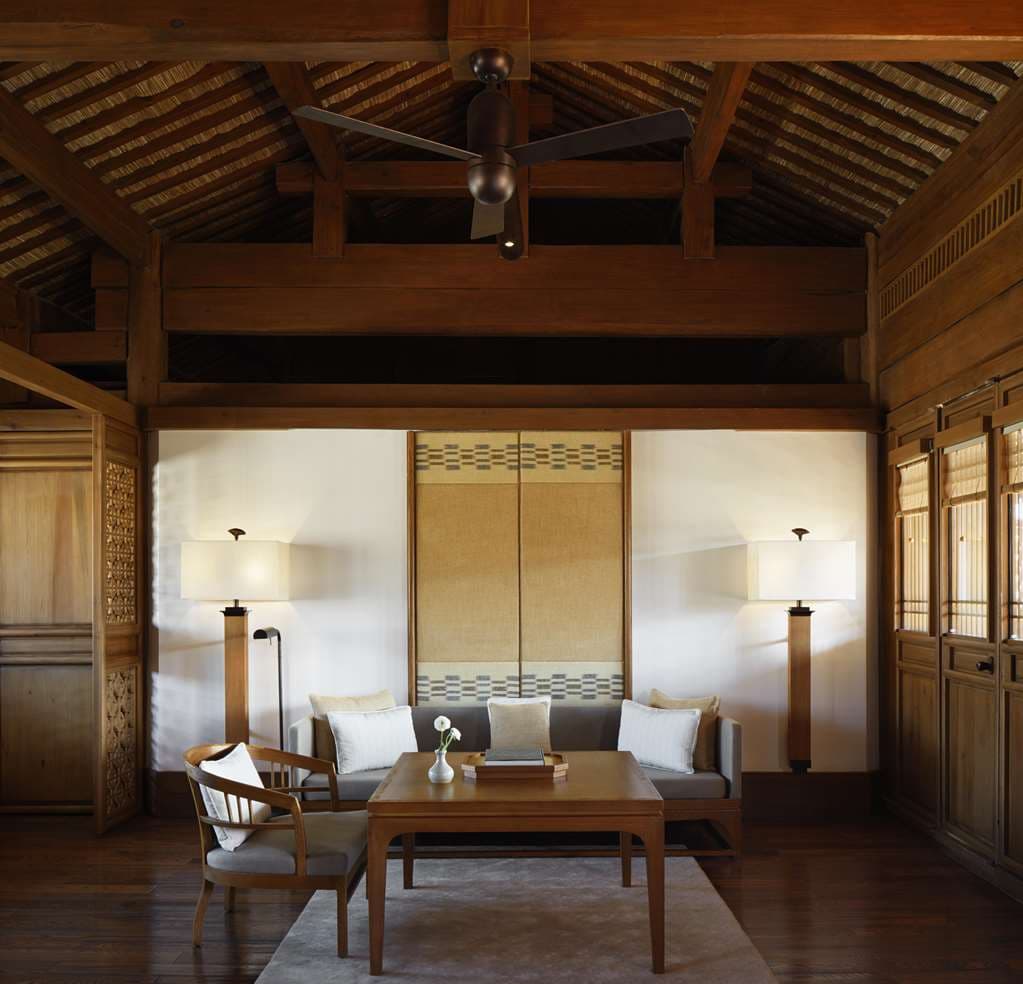 A serene courtyard at Amandayan featuring traditional Naxi architecture with curved tiled roofs, a heated outdoor pool reflecting the sky, and Jade Dragon Snow Mountain in the distance.