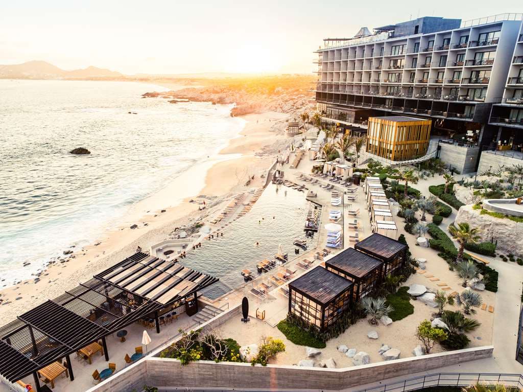 The Cape hotel infinity pool at sunset with views of El Arco rock formation and guests lounging on daybeds.