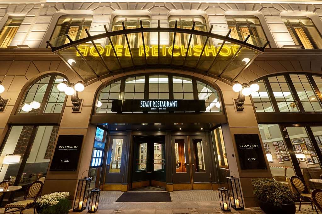 Grand Art Deco lobby of Reichshof Hamburg featuring purple chandeliers, marble columns, and a wrap-around mezzanine gallery.