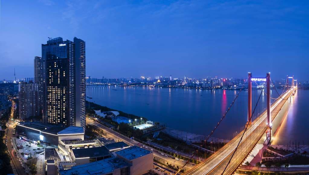 View from Hilton Wuhan Riverside room featuring floor-to-ceiling windows overlooking the Yangtze River and the red Yingwuzhou Suspension Bridge.