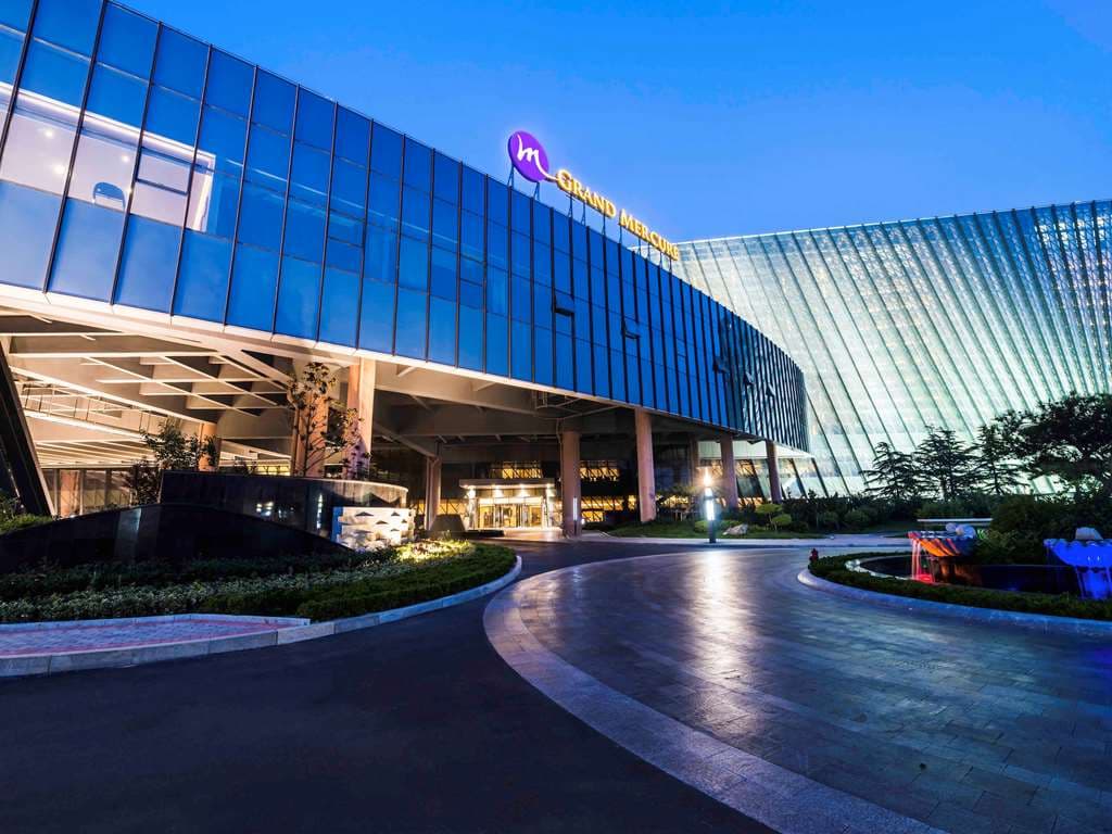 Grand Mercure Qingdao Nanshan Resort lobby featuring high ceilings and marble floors, expansive view of Aoshan Bay at sunset.