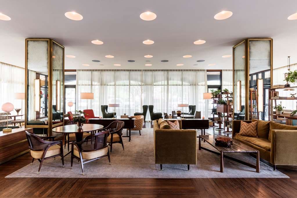 The Living Room bar at The Dewberry Charleston featuring mid-century modern furniture, brass accents, and marble flooring.