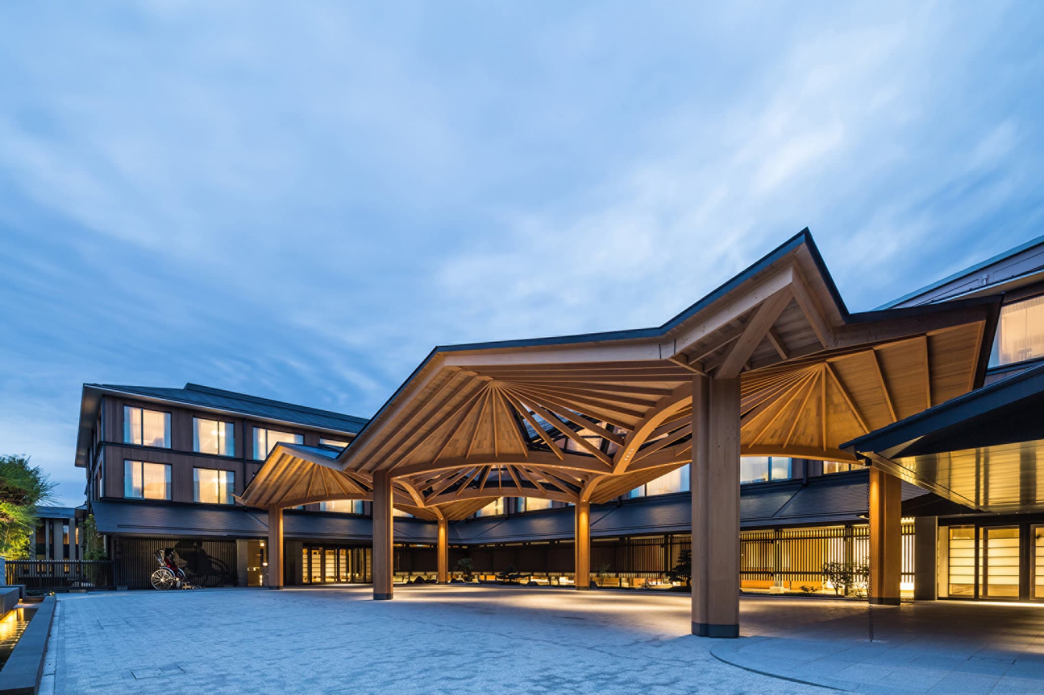 The glass-walled lobby of Four Seasons Kyoto looking out onto the historic Shakusuien pond garden at dusk.
