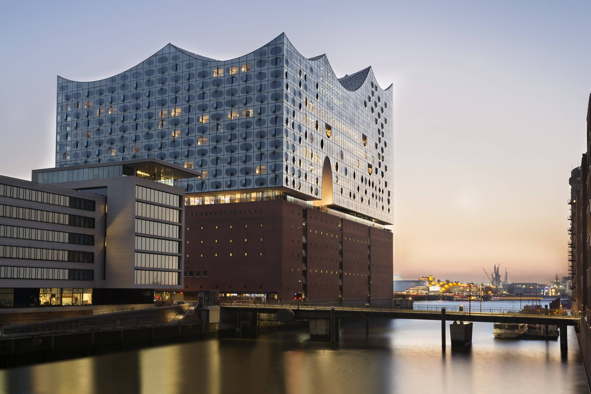 A guest sitting in the curved window nook of The Westin Hamburg overlooking the industrial harbor cranes and Elbe river.