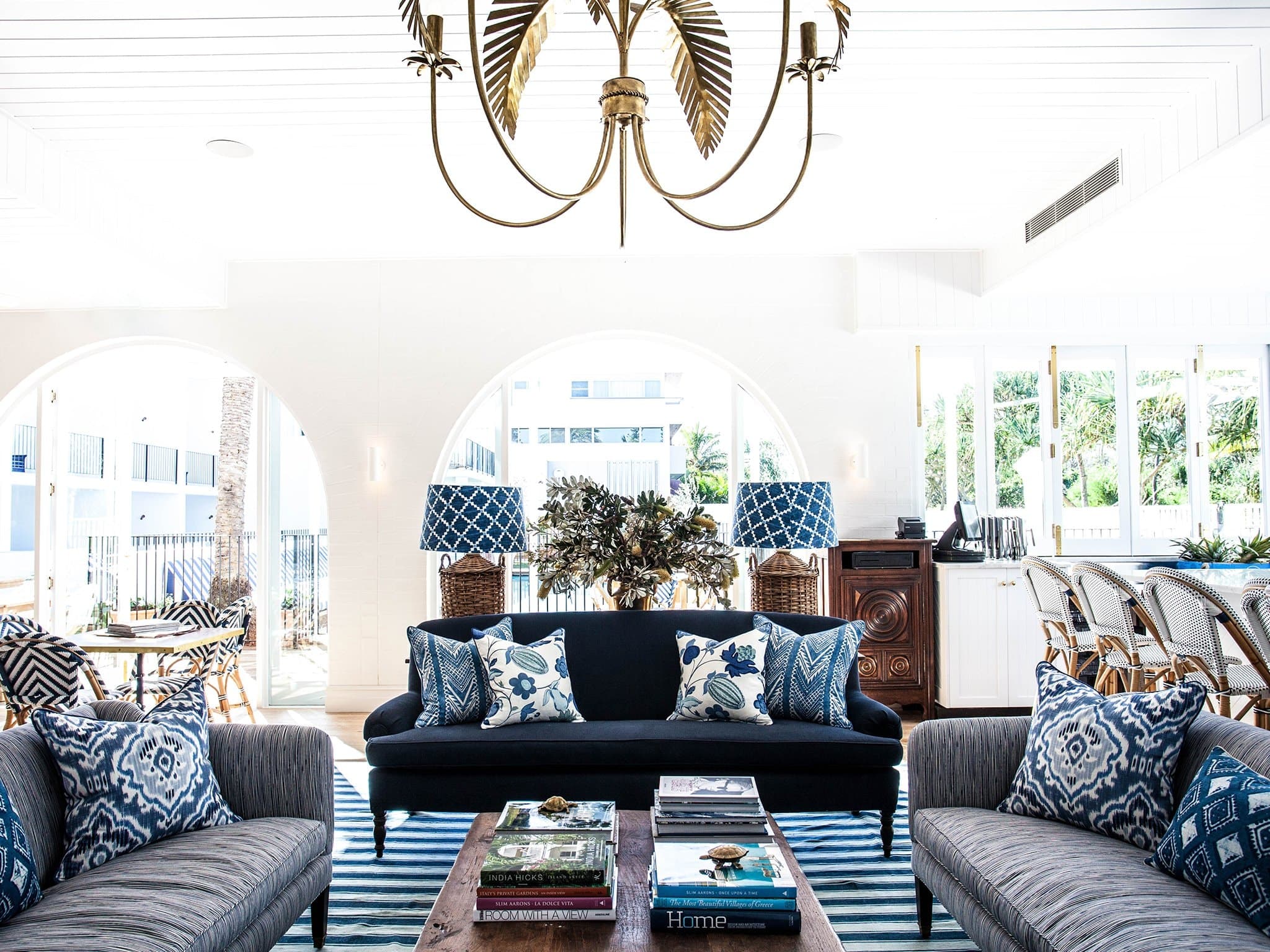 Poolside at Halcyon House with signature blue and white striped loungers and pandanus palms framing the hotel facade.